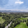 Vista panorámica aérea de un parque con extensas zonas verdes, senderos peatonales, grupos de árboles y un lago en un costado.