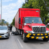 Vehículo de carga rojo y automóvil gris detenidos sobre una vía de Bogotá, junto a una motocicleta caída entre ambos. En el lugar hay presencia de agentes de tránsito y otras personas, con zonas verdes y árboles a los costados de la carretera.