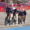 Cuatro ciclistas colombianas compiten en una pista de ciclismo de velódromo, avanzando en formación sobre sus bicicletas de pista mientras usan uniformes azul oscuro y cascos de protección.