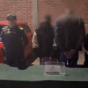 Dos personas capturadas de espaldas y esposados junto a dos policías 