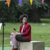 Imagen de una payasa sentanda en un parque que mira tristemente. 