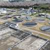 Vista aérea de la PTAR Salitre con múltiples tanques circulares y rectangulares para el tratamiento de aguas residuales, rodeados de estructuras operativas y canales.