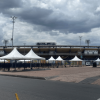 Vista exterior de una terminal de transporte con varias carpas blancas alineadas en la zona de acceso. Al fondo se observa un edificio de varios niveles y un cielo nublado con abundantes nubes grises. En primer plano hay una amplia superficie pavimentada sin presencia visible de personas.