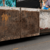 Contenedor metálico de gran tamaño utilizado para la recolección de residuos, ubicado sobre una vía pavimentada.