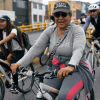 Personas en bicicleta recorren una vía urbana durante una jornada de Ciclovía. En primer plano, una persona vestida con ropa deportiva gris y gorra conduce una bicicleta blanca