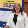 Ciudadana mayor posa en un stand de su emprendimiento en un evento organizado por la Secretaría Distrital de Integración Social, teniendo tras de ella un pendón sobre el programa Ingreso Mínimo Garantizado (IMG).