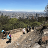 Personas recorren el sendero peatonal de Monserrate entre rocas y vegetación; al fondo se observa una vista panorámica de Bogotá bajo cielo despejado.
