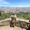 Vista panorámica de Bogotá desde un mirador en Monserrate. En primer plano se observa un muro de piedra y dos visitantes de espaldas contemplando la ciudad.