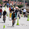 Personas caminando, trotando y montando bicicleta por una vía habilitada para la Ciclovía de Bogotá, delimitada con conos verdes y blancos, sobre un puente urbano durante el día.