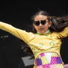 Imagen de una niña porrista con pompones fucsia, blusa amarilla y falda fucsia.