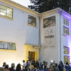 Edificación de tres niveles de la Casona de la Danza iluminada en tonos blancos, amarillos y morados durante el atardecer. Frente al acceso principal se observa un grupo de personas reunidas, mientras en la fachada destaca el nombre “Casona de la Danza”.