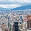 Vista panorámica de Bogotá con edificios residenciales y empresariales, avenidas principales y cerros al fondo bajo un cielo cubierto de nubes grises.