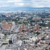 Vista panorámica de Bogotá con áreas residenciales, edificios de diferentes alturas, corredores viales y amplias zonas verdes. Al fondo se observan los cerros y un cielo cubierto de nubes sobre la ciudad.