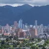 Panorama de Bogotá con vista amplia de edificaciones y rascacielos en el centro de la ciudad, zonas verdes en primer plano y los Cerros Orientales al fondo bajo un cielo parcialmente nublado.
