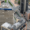 Vista aérea de edificios y vías en el centro de Bogotá. En primer plano destaca un edificio con el letrero “Corfi Colombiana”, rodeado de torres de oficinas, calles con vehículos en circulación y un mural de gran formato en la fachada de un edificio cercano.