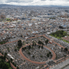 Vista panorámica de Bogotá con edificaciones residenciales y comerciales, corredor vial rodeado de árboles, amplias zonas verdes, cementerio y conjuntos de apartamentos al fondo bajo cielo nublado.