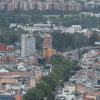Vista panorámica de Bogotá con edificaciones residenciales y comerciales, corredor vial rodeado de árboles, amplias zonas verdes y conjuntos de apartamentos al fondo bajo cielo nublado.