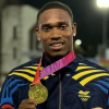 Ronal Longa sostiene una medalla dorada frente a una pista de atletismo iluminada durante la noche. En la prenda se observa el logo del Comité Olímpico Colombiano.