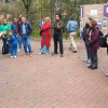 Personas participan en una actividad al aire libre sobre una plazoleta de ladrillo. Varias están alineadas y observan una demostración; algunas llevan chaquetas azules y una persona en el centro viste una chaqueta roja.