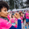 Participante de la Carrera de la Mujer con camiseta rosada y audífonos alrededor del cuello, entre corredoras reunidas en la zona de encuentro previa a la competencia.