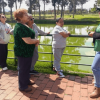 Participantes de una jornada comunitaria de siembra en el parque Timiza sostienen herramientas y materiales de jardinería junto a un área verde delimitada para la plantación de árboles y arbustos.