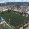 Vista aérea de una cancha sintética de fútbol rodeada por viviendas y edificaciones urbanas en Bogotá.