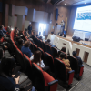 Asistentes participan en una jornada de socialización del Plan de Acción Acústico de Bogotá en un auditorio, mientras una presentación se proyecta en pantalla principal.