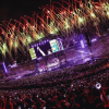 BTS en concierto en Bogotá con vista panorámica del estadio El Campín lleno de asistentes. En el escenario central hay pantallas gigantes y sobre el recinto se observan fuegos artificiales de colores que iluminan al público y las graderías.