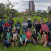 Grupo de personas posa para una fotografía al aire libre sobre una zona con césped. Varias personas llevan chalecos, gorras y prendas de colores llamativos, mientras algunas sostienen herramientas utilizadas en actividades de jardinería o mantenimiento vegetal.