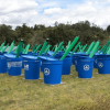 Canecas azules de la CAR Cundinamarca para almacenamiento de agua alineadas sobre un terreno cubierto de césped, junto a estructuras verdes instaladas como parte de un sistema de recolección y aprovechamiento de agua en zona rural.