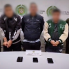 Foto de tres hombres capturados por la policía, escoltados por dos oficiales, uno en cada costado. 