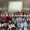 Grupo de estudiantes y docentes de Teusaquillo posa para una fotografía grupal en un espacio interior de un colegio. Al fondo se observa una pantalla de proyección y un muro de ladrillo, mientras los participantes están ubicados en varias filas frente a la cámara