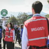 Brigadistas de la Cruz Roja Bogotá orientan un ejercicio de preparación para emergencias mientras varias personas sostienen señales de punto de encuentro en un espacio abierto.
