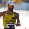 Eider Arévalo Deportista de marcha atlética con uniforme amarillo de la selección Colombia durante una competencia. Lleva gafas deportivas, gorra clara y un número de competencia visible en el pecho, mientras avanza por el circuito.