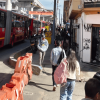 Peatones caminando por una acera junto a autobuses articulados rojos de TransMilenio en una concurrida vía urbana de Bogotá.