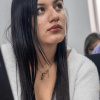 Foto de una mujer con otras dos de fondo, en un salón de clases.