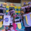 Grupo de personas posando en un centro comercial durante un concurso de disfraces. Dos personas llevan disfraces de cocodrilo hechos con cartones de huevera pintados de verde, con grandes mandíbulas abiertas, dientes blancos y ojos saltones.