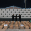 Foto de una persona capturada en medio de dos policías, con e cargamento de 700 kg de marihuana expuestos en el piso. 