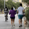 Personas caminando, corriendo y montando en bicicleta por una vía urbana cerrada al tráfico durante una jornada recreativa. Varias bicicletas circulan por la calzada y dos perros acompañan a los participantes en la Ciclovía de Bogotá.