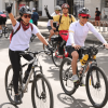 Personas participan en la Ciclovía de Bogotá recorriendo una vía urbana en bicicleta. En primer plano, varias personas usan casco y pedalean por la calzada, mientras otras ciclistas avanzan detrás.