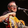 Imagen del cantante César López en un escenario donde lleva una guitarra en sus manos.