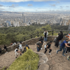 Vista panorámica de Bogotá desde un mirador en la montaña. Varias personas recorren y descansan en el sendero de Monserrate rodeado de vegetación