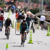 Personas caminan, trotan y montan bicicleta por una vía de la Ciclovía de Bogotá, delimitada con conos, mientras otras permanecen a los costados del recorrido.