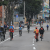 Ciclistas y peatones transitan por una vía de la Ciclovía de Bogotá, rodeados de árboles y edificaciones urbanas durante una jornada recreativa al aire libre