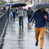 Personas caminan bajo la lluvia por una vía de Bogotá mientras una de ellas sostiene una sombrilla negra y otras transitan por un andén mojado durante fenómeno de El Niño 2026.