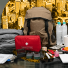 Kit de emergencias sobre una mesa con una mochila gris, botiquín rojo, linterna, pilas, radio portátil, alimentos no perecederos, botellas de agua y otros elementos recomendados para atender una emergencia.