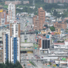 Vista panorámica de un sector urbano de Bogotá con edificios residenciales y comerciales de diferentes alturas, una vía principal con tráfico vehicular y construcciones densamente distribuidas en el paisaje urbano.