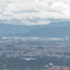 Vista panorámica de Bogotá desde un punto elevado. En primer plano se observan edificaciones urbanas y, al fondo, una cadena montañosa bajo un cielo con abundante nubosidad.
