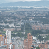 Vista panorámica de Bogotá desde un punto elevado. En primer plano se observan edificios residenciales y comerciales, mientras al fondo se extiende la ciudad bajo un cielo nublado con montañas en el horizonte.