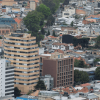 Vista panorámica de una zona urbana de Bogotá con edificios residenciales y comerciales de diferentes alturas. En primer plano destacan una torre de color beige con balcones curvos y un edificio de ladrillo rojo.